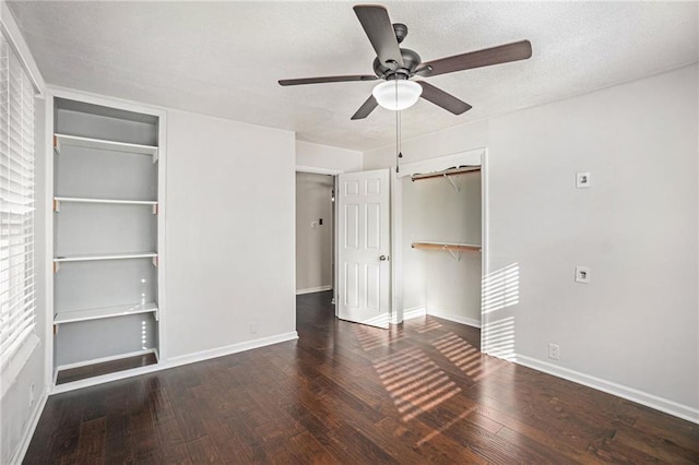 unfurnished bedroom with two closets, a textured ceiling, baseboards, and hardwood / wood-style floors