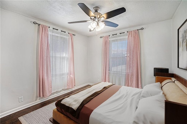bedroom with dark wood-type flooring, a ceiling fan, baseboards, and a textured ceiling