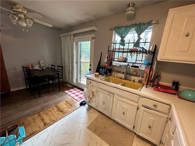 kitchen with light wood-style flooring, a sink, ceiling fan, light countertops, and white cabinetry