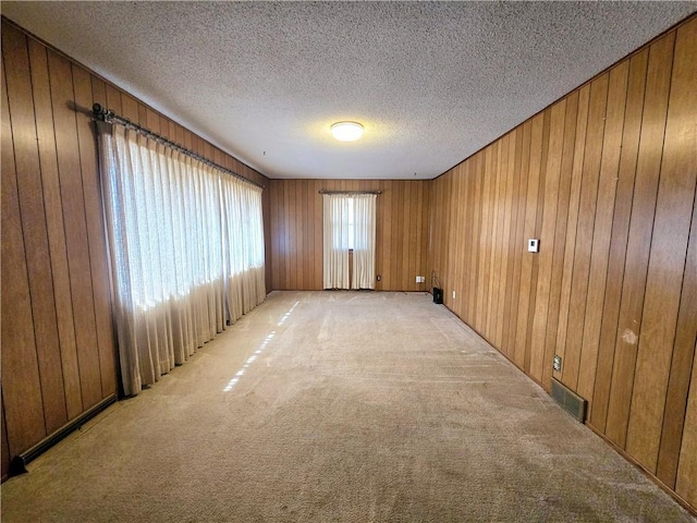 empty room featuring visible vents, wood walls, light colored carpet, and a textured ceiling