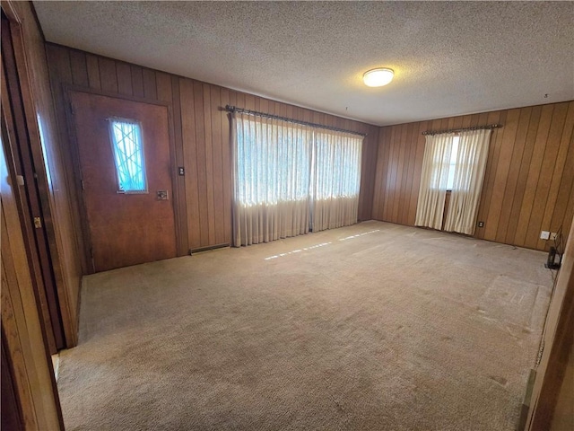 interior space featuring wooden walls, light colored carpet, and a textured ceiling