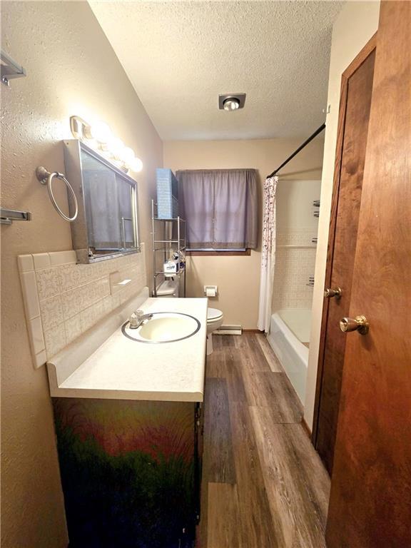 full bathroom with vanity, shower / tub combo with curtain, toilet, a textured ceiling, and wood finished floors