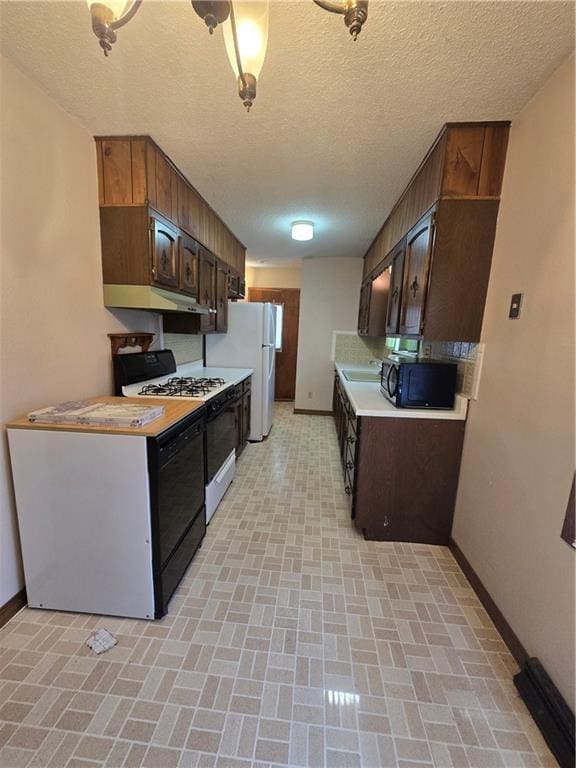 kitchen featuring light countertops, under cabinet range hood, baseboards, brick patterned floor, and black appliances