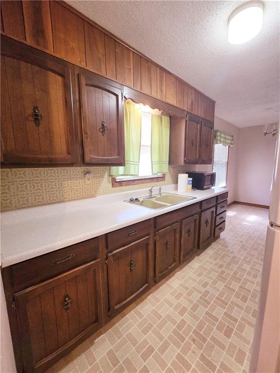 kitchen with brick floor, light countertops, decorative backsplash, and a sink