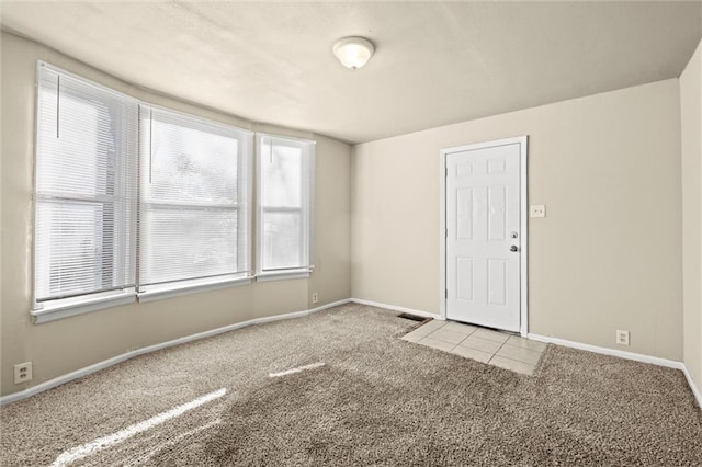 carpeted spare room featuring tile patterned floors, visible vents, and baseboards