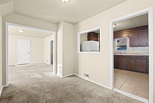 hall featuring visible vents, a sink, light tile patterned floors, baseboards, and light colored carpet