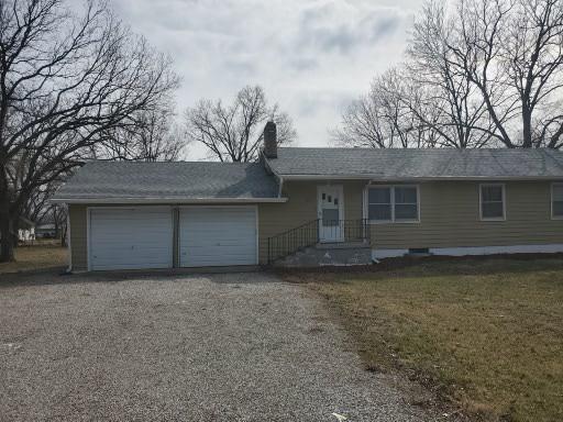 ranch-style home featuring a garage, gravel driveway, and a chimney