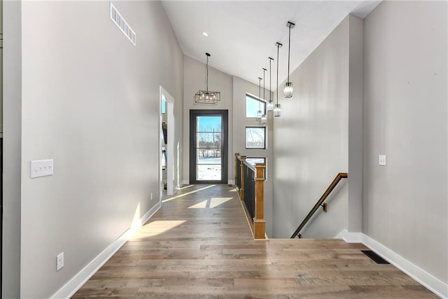 foyer entrance featuring baseboards, wood finished floors, visible vents, and high vaulted ceiling