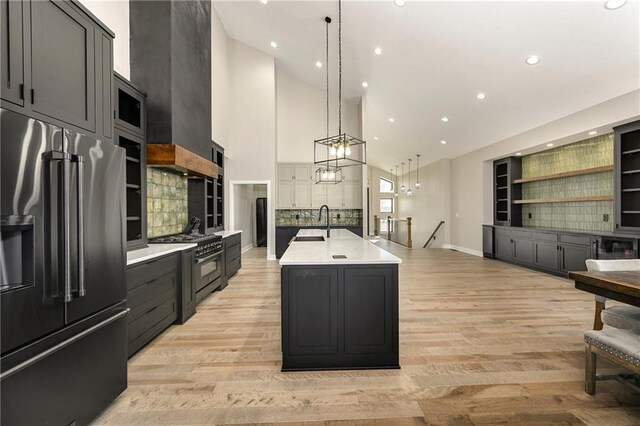 kitchen with light wood finished floors, a sink, light countertops, wall chimney range hood, and premium appliances