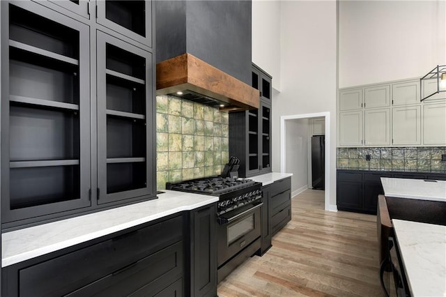 kitchen with light wood finished floors, custom range hood, decorative backsplash, a towering ceiling, and black appliances