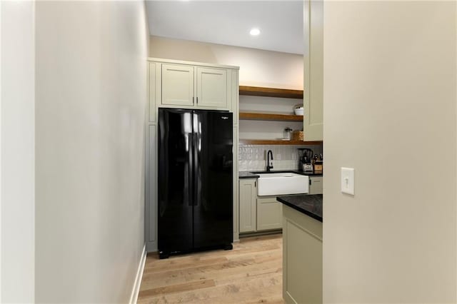 kitchen with a sink, open shelves, dark countertops, freestanding refrigerator, and decorative backsplash