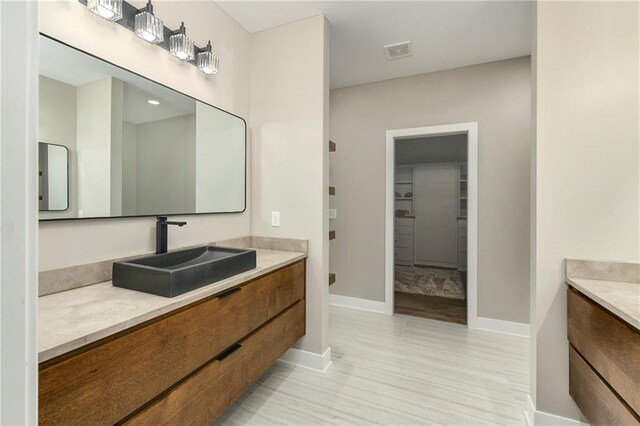 full bath featuring a spacious closet, visible vents, baseboards, wood finished floors, and vanity