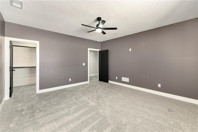 unfurnished bedroom featuring carpet, baseboards, ceiling fan, a textured ceiling, and a walk in closet