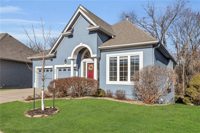 traditional-style house featuring a front yard, roof with shingles, driveway, and stucco siding