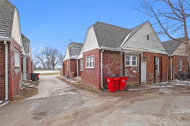 view of side of home featuring a shingled roof, cooling unit, and brick siding