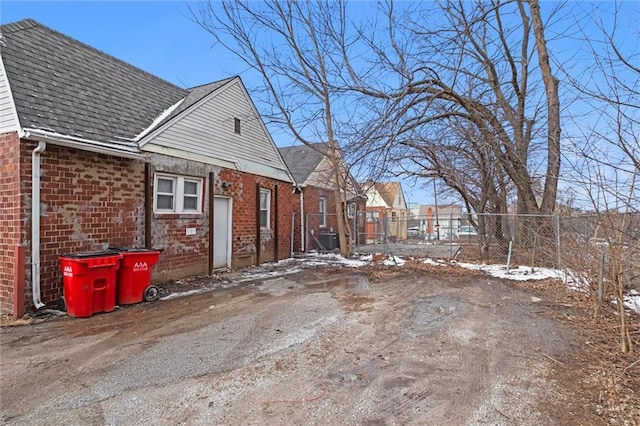 view of snow covered exterior featuring brick siding, roof with shingles, and fence