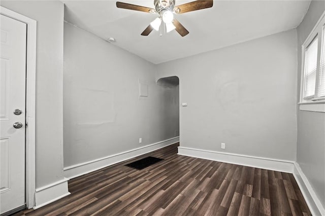 spare room with baseboards, visible vents, a ceiling fan, arched walkways, and dark wood-style flooring