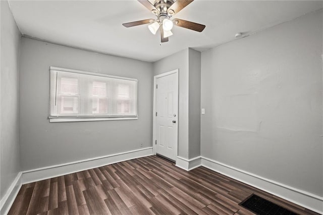 spare room with a ceiling fan, visible vents, baseboards, and dark wood-type flooring