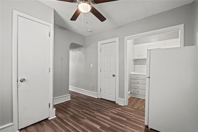 unfurnished bedroom featuring dark wood-style floors, a ceiling fan, freestanding refrigerator, and baseboards