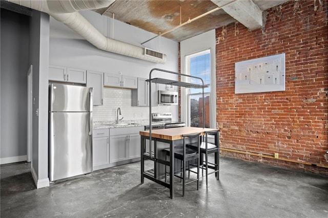 kitchen featuring a sink, concrete floors, appliances with stainless steel finishes, and brick wall