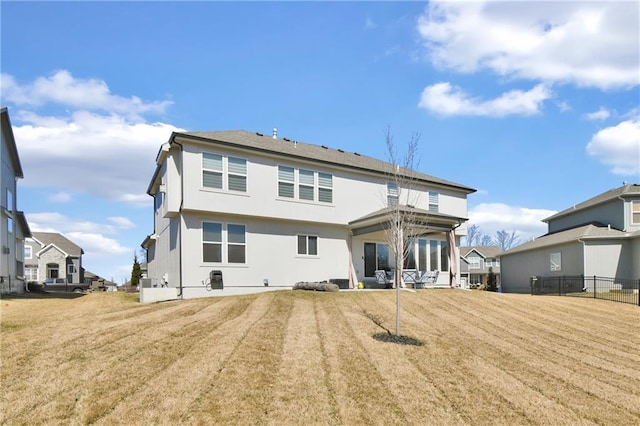 rear view of property featuring a yard, fence, and stucco siding