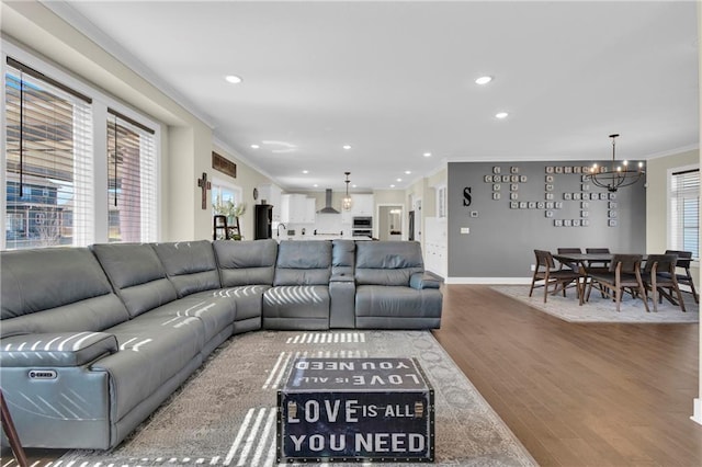 living area with crown molding, a notable chandelier, wood finished floors, and plenty of natural light