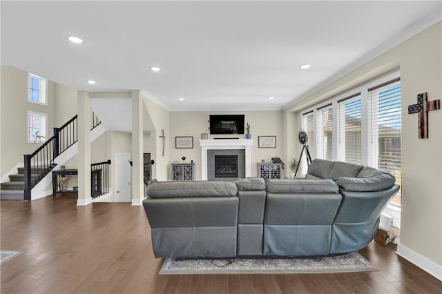 living room featuring dark wood-style floors, baseboards, stairs, a glass covered fireplace, and crown molding