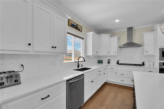 kitchen featuring ornamental molding, a sink, white cabinets, appliances with stainless steel finishes, and wall chimney range hood