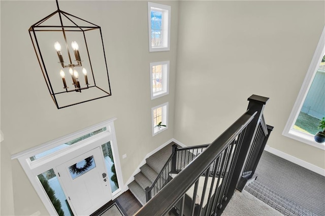 staircase featuring a notable chandelier, baseboards, carpet, and a towering ceiling