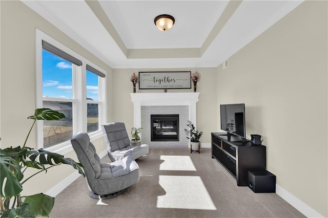 interior space featuring a tray ceiling, baseboards, a brick fireplace, and carpet flooring