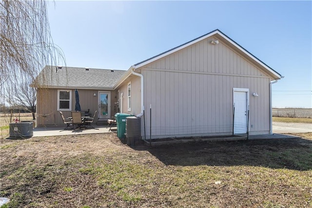 rear view of property with a patio area, central AC unit, a lawn, and roof with shingles