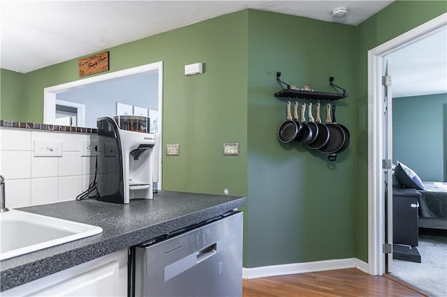 kitchen featuring dark countertops, tasteful backsplash, stainless steel dishwasher, white cabinetry, and a sink