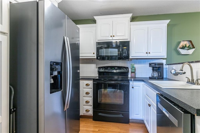 kitchen featuring light wood-type flooring, black appliances, a sink, dark countertops, and white cabinetry