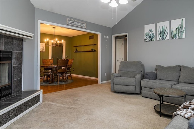 carpeted living room featuring a tiled fireplace, lofted ceiling, ceiling fan with notable chandelier, and baseboards