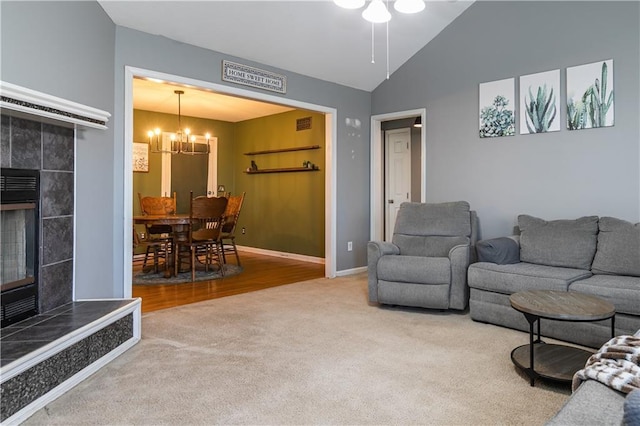 living area featuring lofted ceiling, ceiling fan with notable chandelier, carpet flooring, baseboards, and a tile fireplace