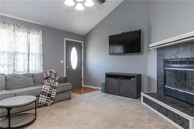 living room featuring baseboards, carpet floors, lofted ceiling, a tile fireplace, and ceiling fan