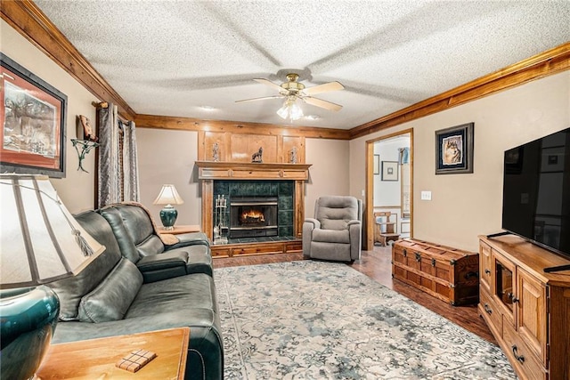 living area featuring a textured ceiling, wood finished floors, crown molding, and a tiled fireplace