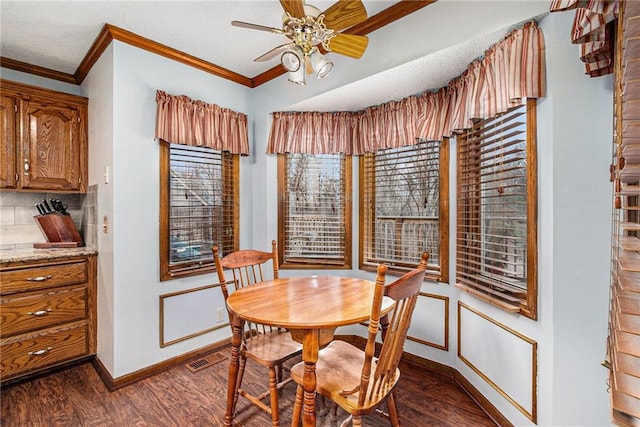 dining room with visible vents, dark wood-type flooring, a ceiling fan, crown molding, and baseboards