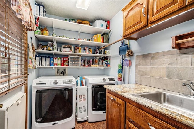 laundry area featuring light wood-style flooring, cabinet space, a sink, a textured ceiling, and washing machine and dryer