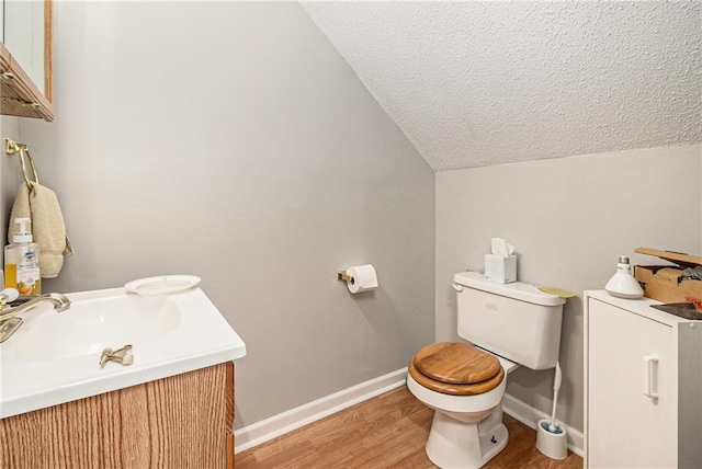 half bathroom with wood finished floors, baseboards, lofted ceiling, a sink, and toilet