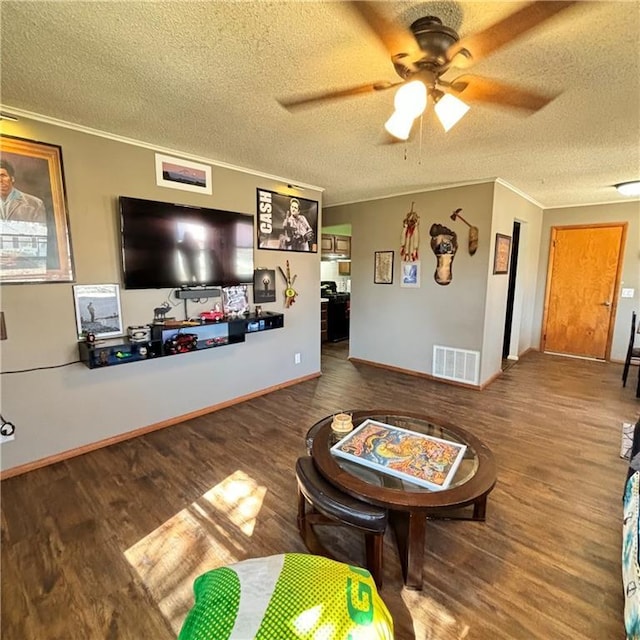 living area with a textured ceiling, wood finished floors, a ceiling fan, visible vents, and crown molding