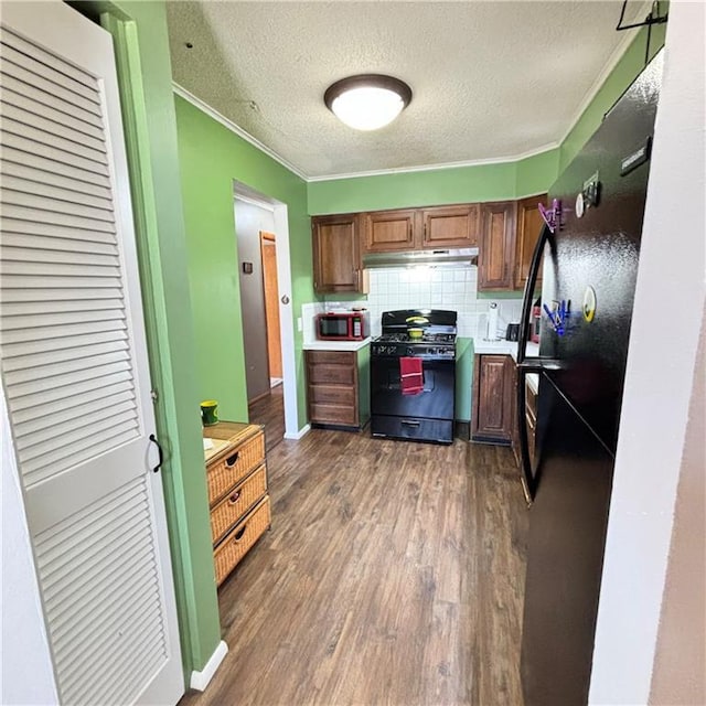 kitchen featuring under cabinet range hood, freestanding refrigerator, decorative backsplash, dark wood-style floors, and gas range