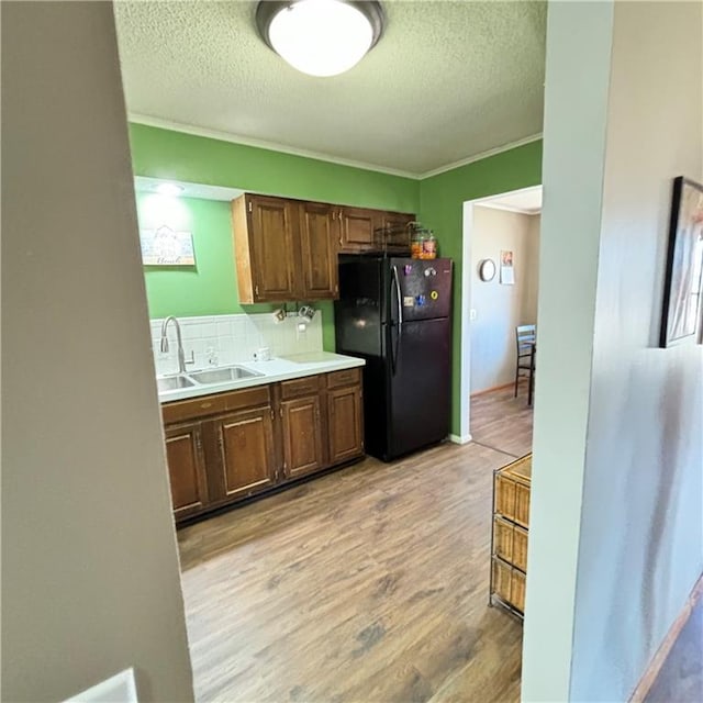 kitchen with freestanding refrigerator, light countertops, a textured ceiling, light wood-type flooring, and a sink