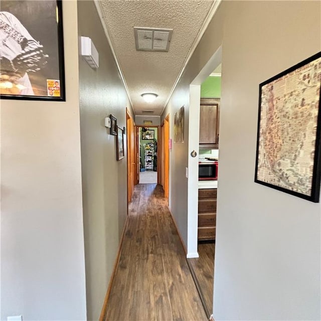 corridor featuring dark wood-style flooring, crown molding, a textured ceiling, and baseboards