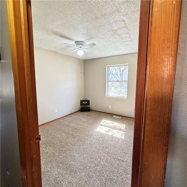 carpeted spare room with ceiling fan, a textured ceiling, and baseboards