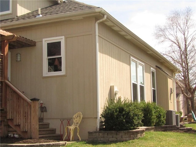 view of home's exterior with stairway, a lawn, a shingled roof, and cooling unit
