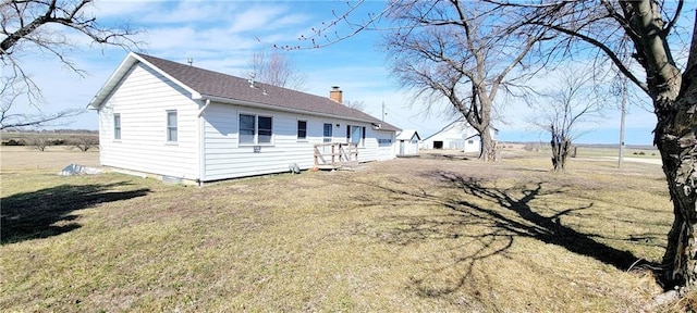 rear view of house featuring a shingled roof, a lawn, and a chimney