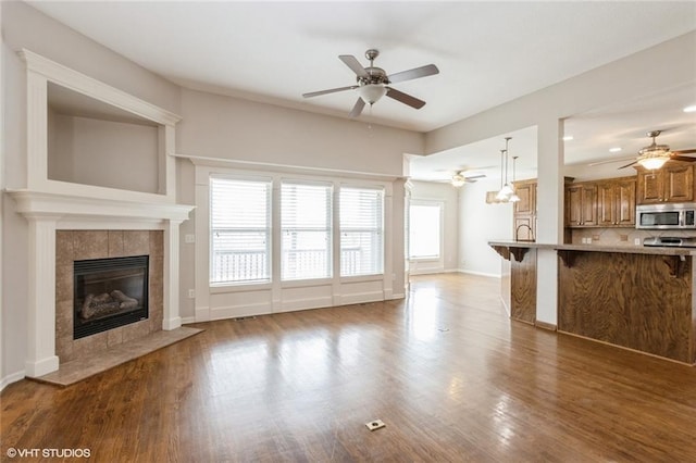 unfurnished living room with a fireplace, baseboards, ceiling fan, and wood finished floors