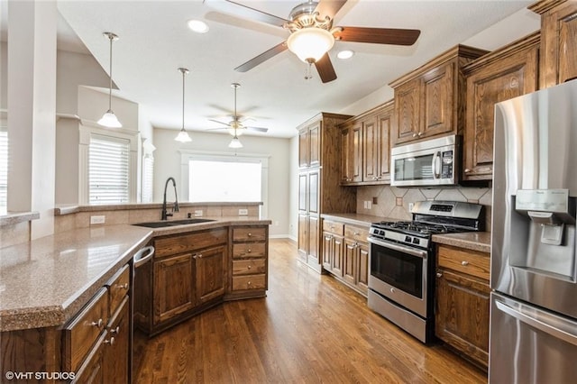kitchen featuring a ceiling fan, dark wood finished floors, a sink, decorative backsplash, and stainless steel appliances