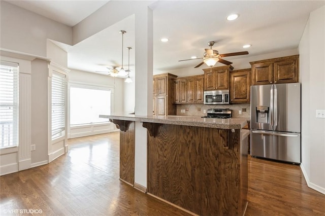 kitchen with a wealth of natural light, a kitchen breakfast bar, appliances with stainless steel finishes, and ceiling fan